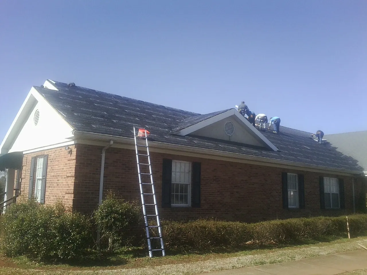 Crew tearing shingles off a brick ranch roof with a ladder set — Metal Roof Repair work by our crew in Hagarville