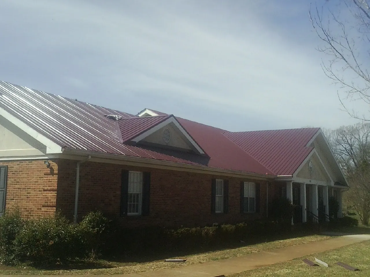 Red metal roof with gabled entries on a long brick building, from a Hail Damage Roof Repair job in Hagarville