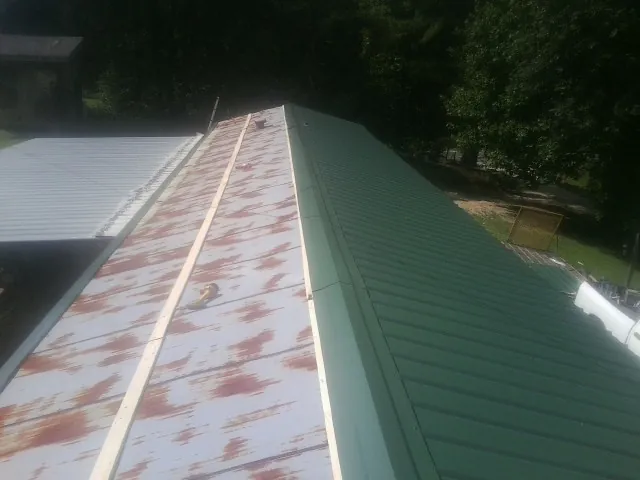 Old rusted panels beside newly installed green metal roofing — Wind Damage Roof Repair by Roofing Brothers in Hagarville