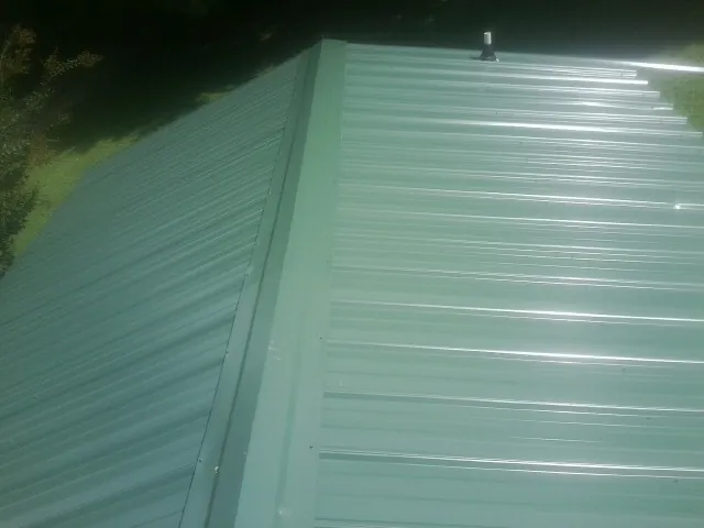 New green metal panels meeting at the ridge of a roof — Flat Roof Repair work by our crew in Hagarville