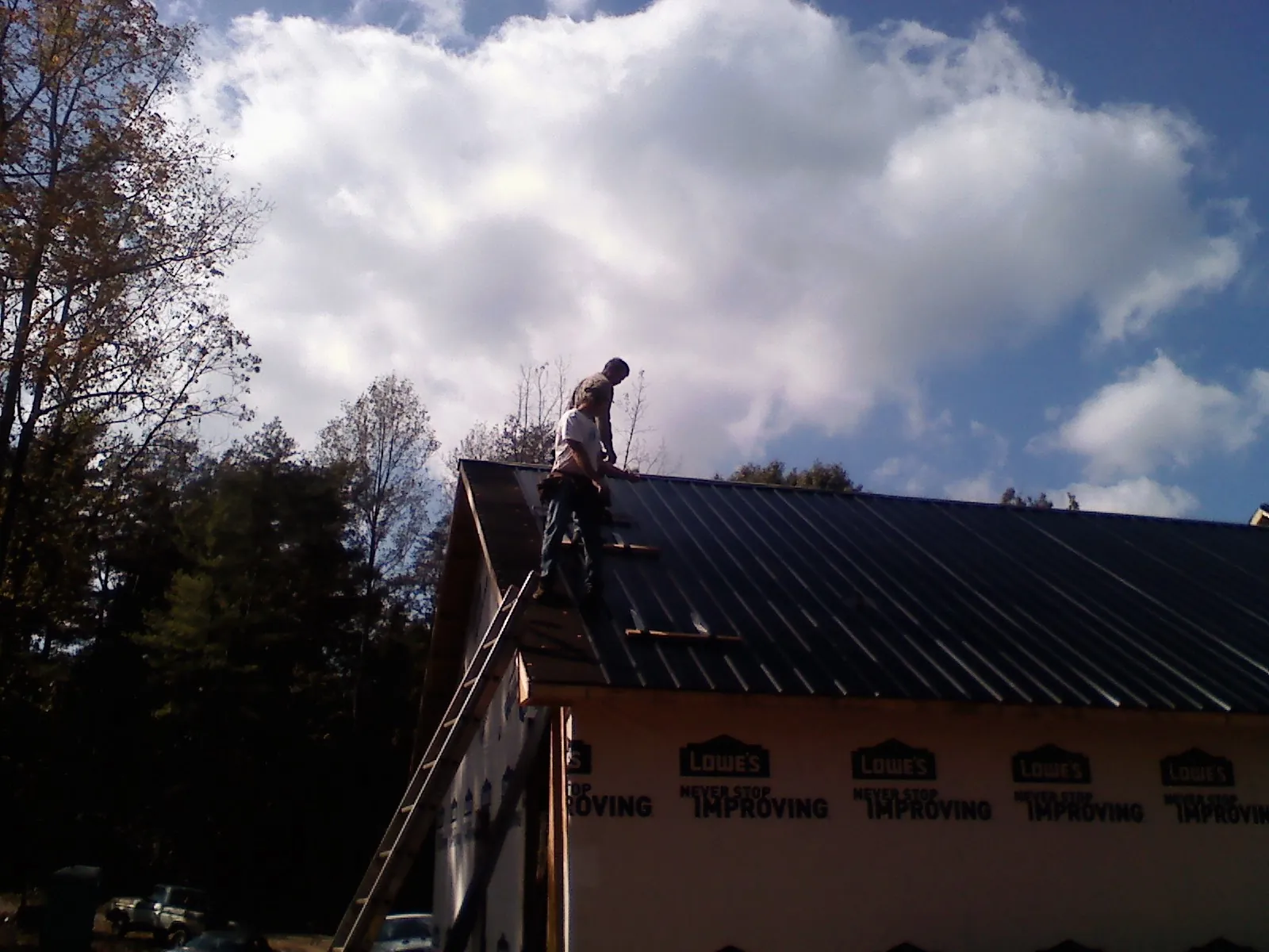 Roofer fastening dark metal panels high against a cloudy sky, from a Roof Inspection job in Hagarville