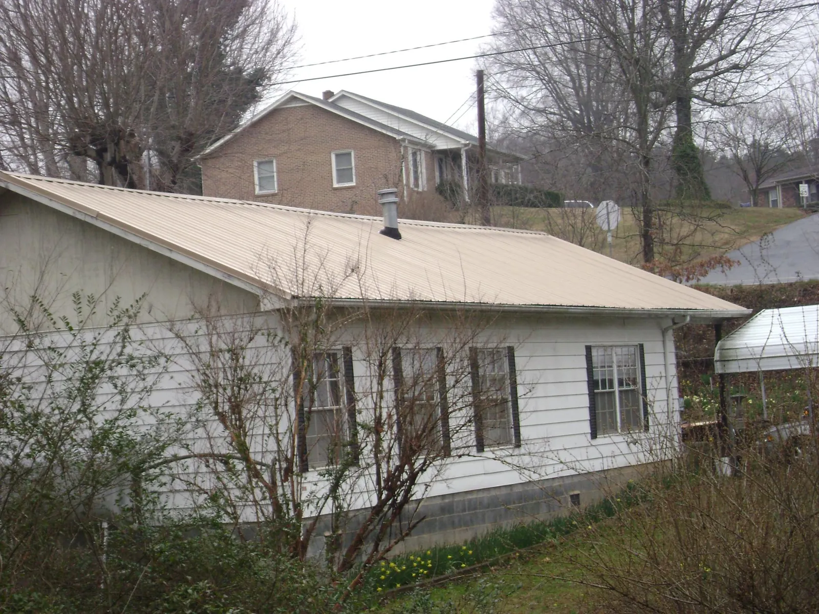 Tan metal roof on a white sided house set into a hillside — Commercial Roofing by Roofing Brothers in Hagarville